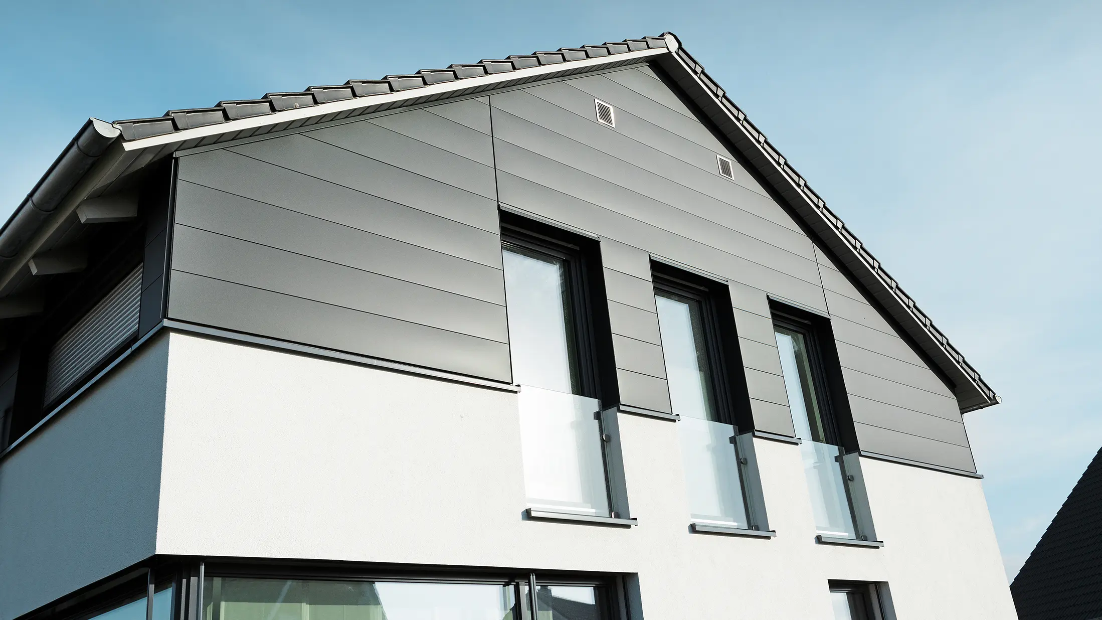 Moderna fasada kuće u Isenbüttelu s PREFA Siding fasadnim kasetama u boji P.10 antracit – aluminijumska obloga daje porodičnoj kući elegantan izgled te dojam otpornosti na vremenske uslove. Vertikalni prozori dodatno naglašavaju modernu arhitekturu.