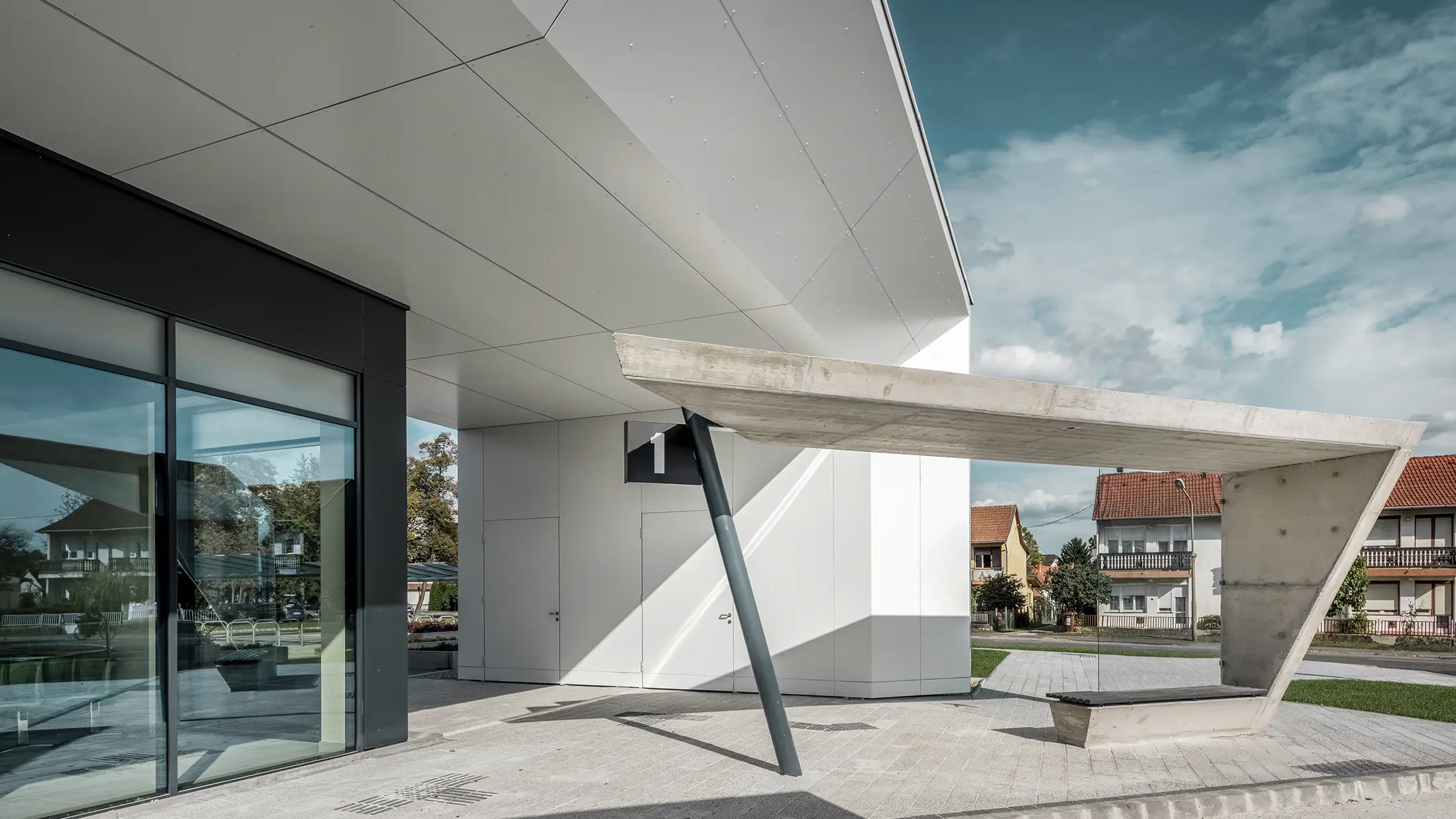 Eingangsbereich des Busbahnhofs Lenti; die Untersicht der Überdachung ist mit der PREFABOND Aluminium Verbundplatte von PREFA in Reinweiß verkleidet, die Fassadenelemente bei den Eingangstüren und Schaufenstern ist in P.10 anthrazit verkleidet.