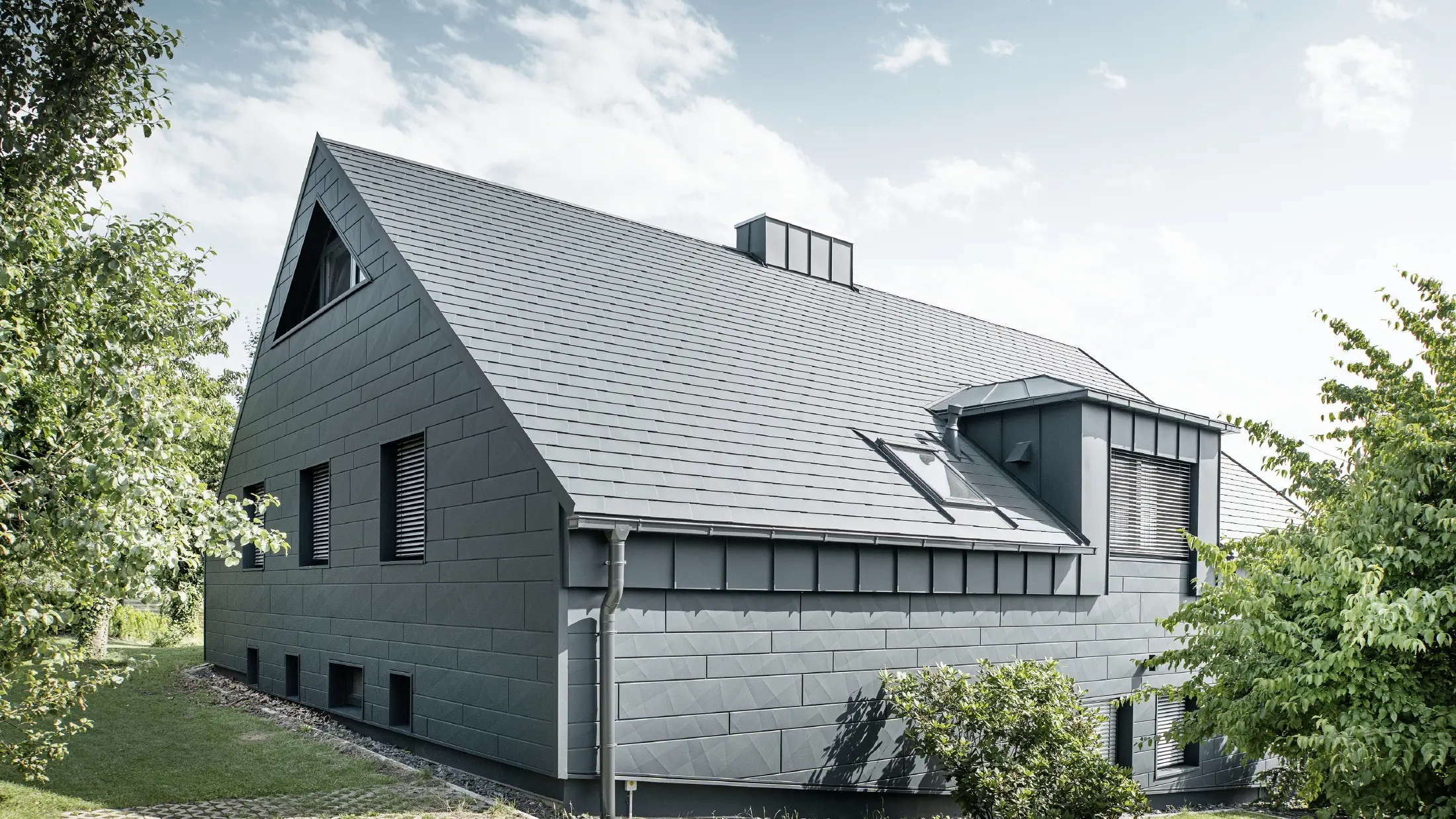Großes Einfamilienhaus mit Satteldach und vielen Fenstern. Das gesamte Haus wurde mit einer Aluminiumhülle in Anthrazit verkleidet, am Dach kamen PREFA Alu-Dachschindeln zum Einsatz und an der Fassade Siding.X in Anthrazit.