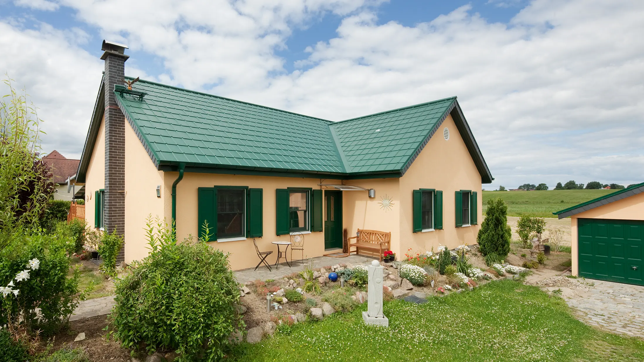 Atraktivan ukupni izgled porodične kuće u Friedrichswaldeu ističe postojani aluminijumski krov u mahovinasto zelenoj boji, koji krasi i kuću i garažu. Zelena nijansa PREFA krovnih ploča skladno se uklapa u prirodno okruženje i naglašava jednostavnu arhitekturu kuće. Prošireni dvovodni krov u obliku slova L nalazi se ispred polja. Šarmantna kućica ima odgovarajuće zelene kapke na prozorima i lijep mali prednji vrt.